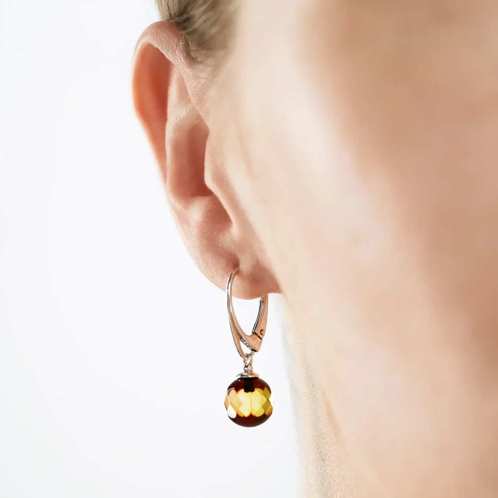 Silver hoop earring with warm amber drop on a womans ear, stylish and elegant accessory.