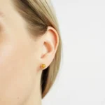 Close-up of a womans ear with elegant yellow gemstone stud earring, showcasing minimalist jewelry style.
