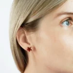 Close-up of red star-shaped amber earrings on a womans ear, showcasing modern jewelry style.