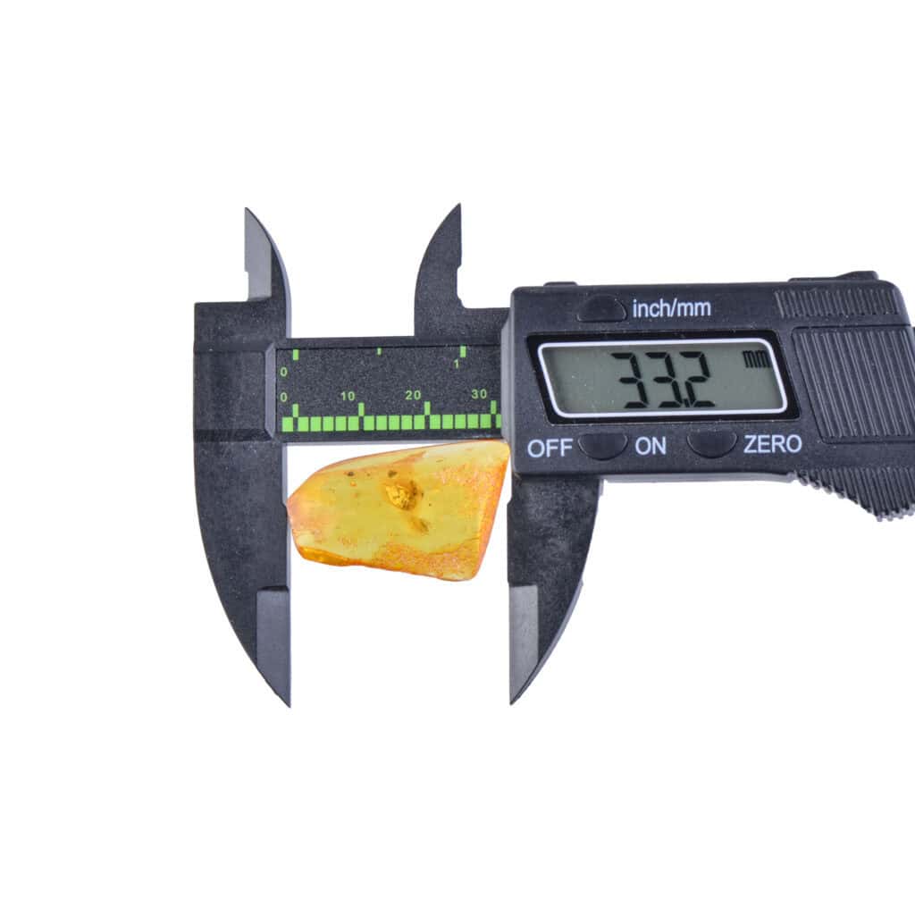 Digital caliper measuring a small amber piece with natural inclusions, showing a 33.2 mm reading.