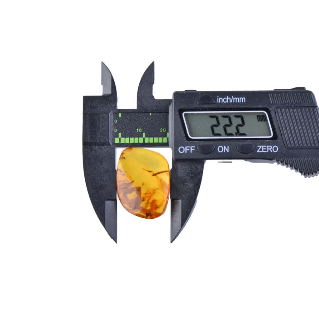 Digital caliper measuring polished amber gemstone, highlighting precision in natural jewelry assessment.