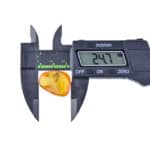 Digital caliper measuring transparent amber, showing 24.7 mm width, highlighting precision and natural beauty.