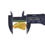 Measuring natural Baltic amber with digital caliper, showing 43.7 mm for precise jewelry crafting.