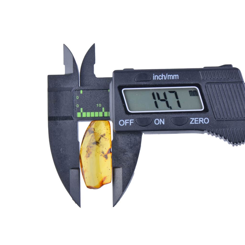 Digital caliper measuring amber gemstone, displaying a 14.7mm width in precise detail.