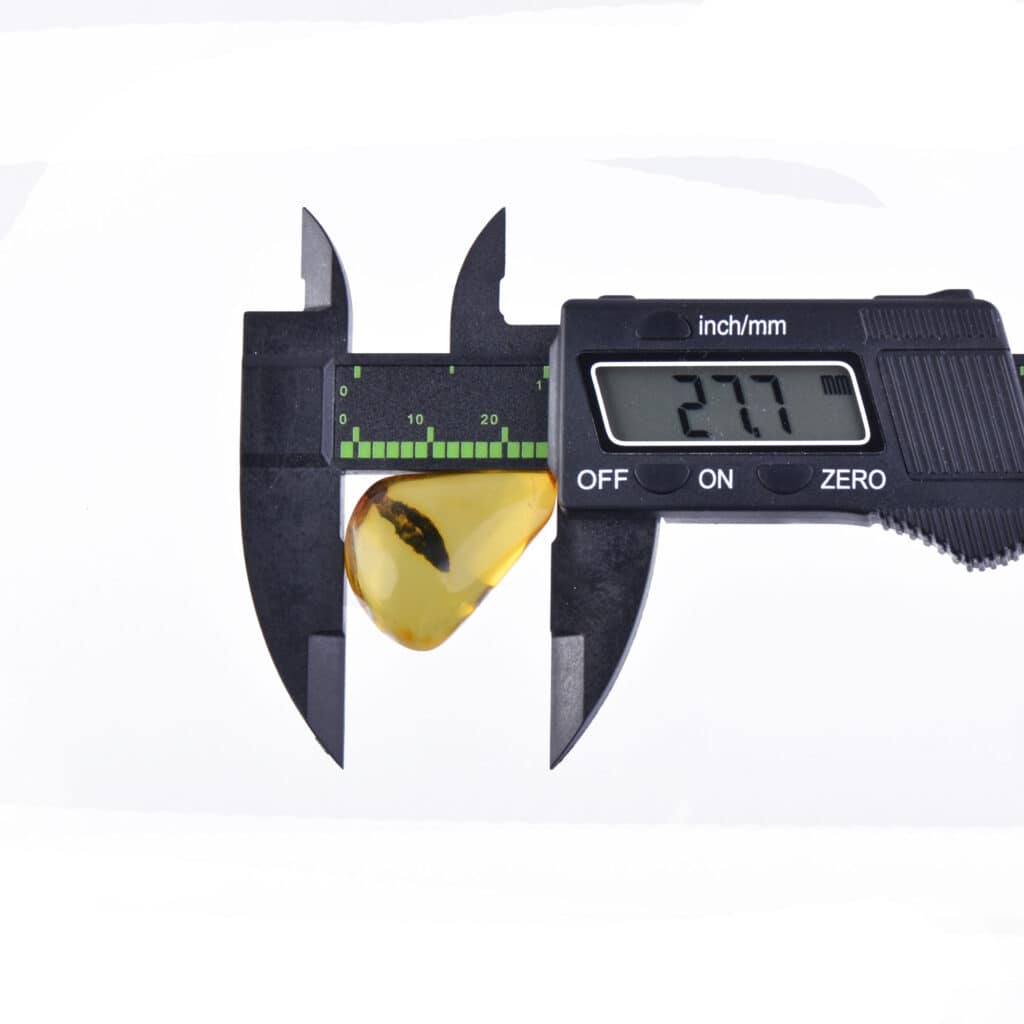 Digital caliper measuring a golden-yellow amber piece with a 2.77mm reading.