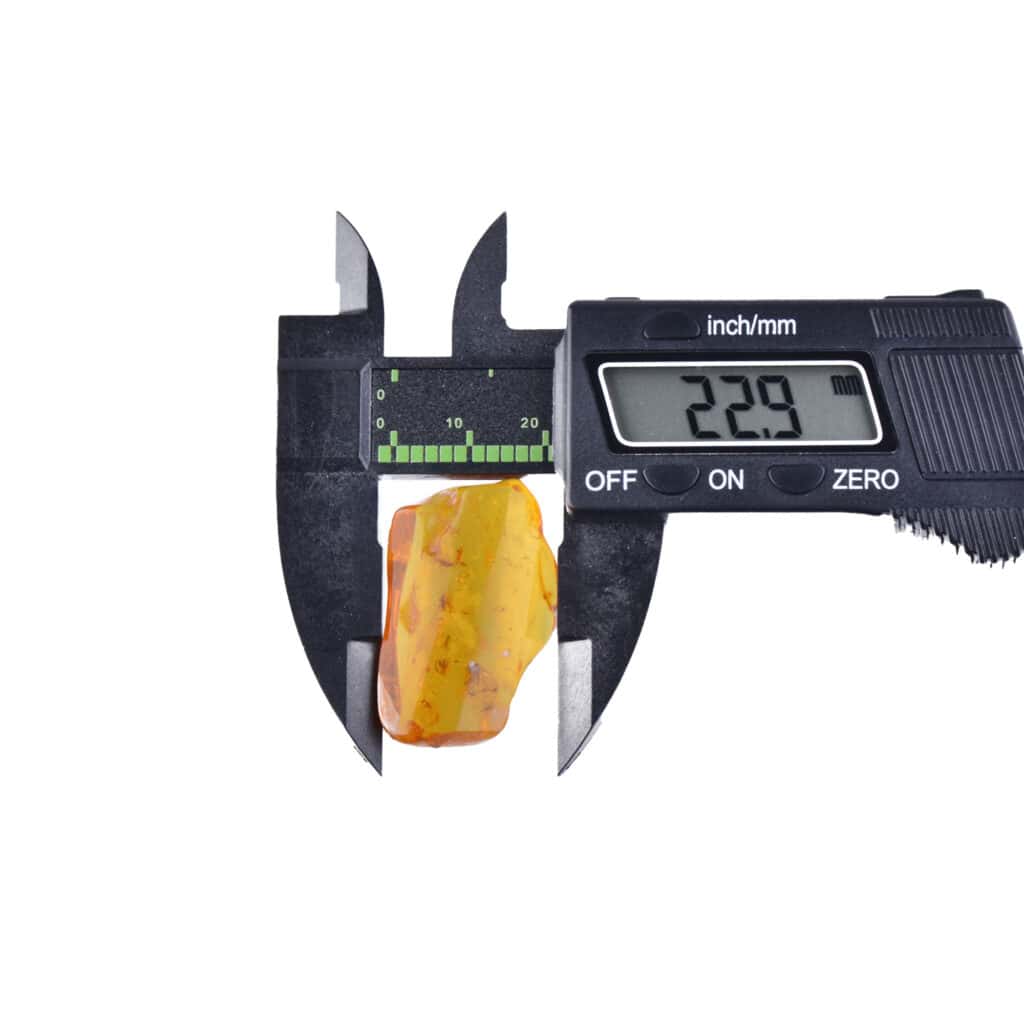 Digital caliper measuring a small amber piece with inclusions, highlighting craftsmanship and natural beauty.