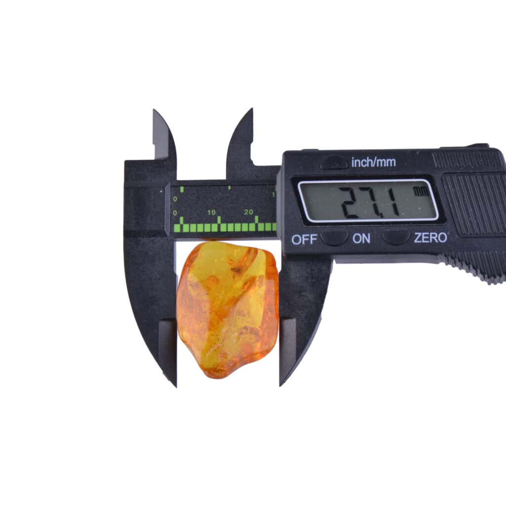 Digital caliper measuring a small, translucent amber piece with natural organic shape and warm orange hue.
