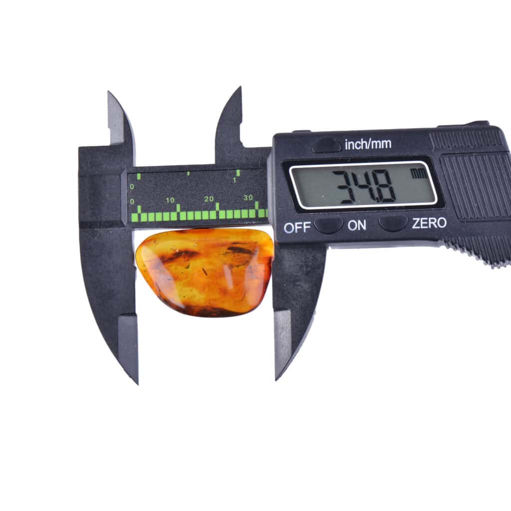 Measuring Baltic amber with digital caliper, showcasing precise size and natural inclusions.