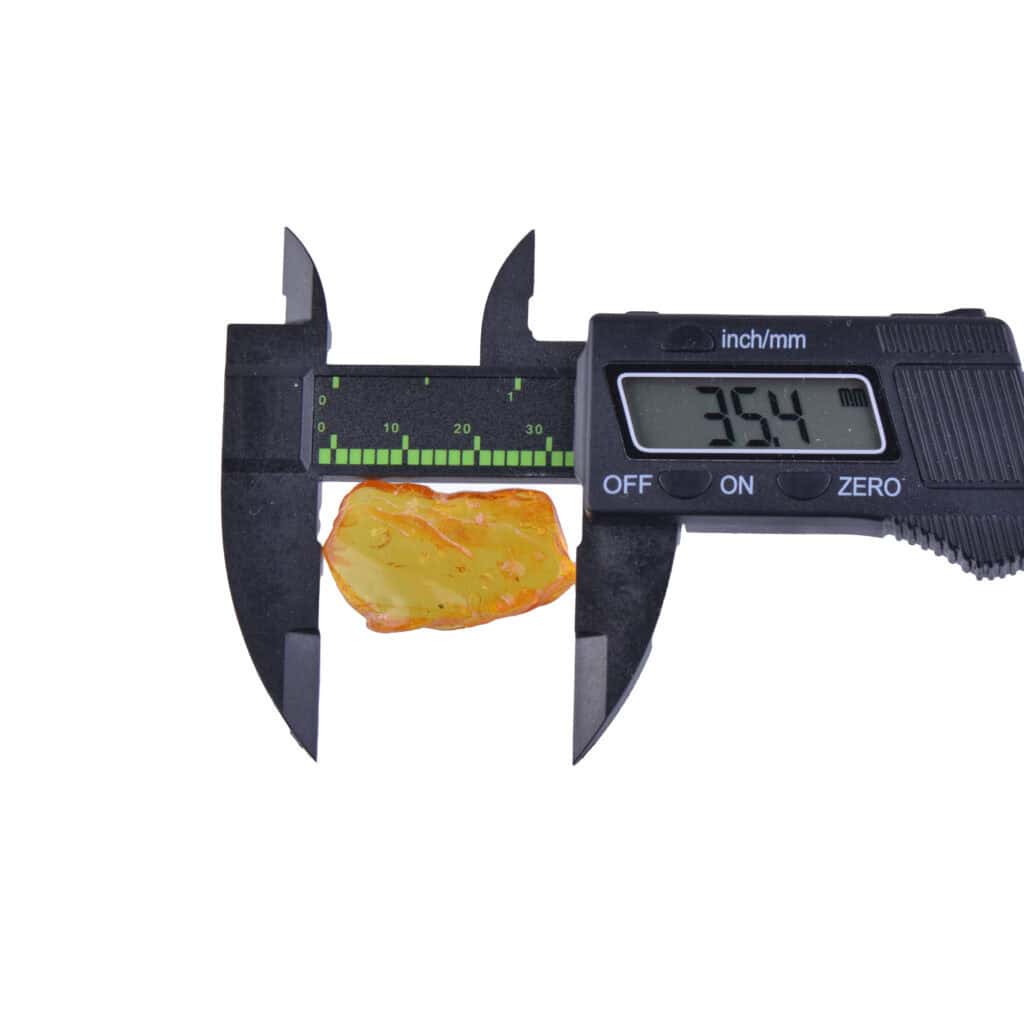 Digital caliper measuring yellowish-orange amber fragment with natural inclusions, 35.4mm size.