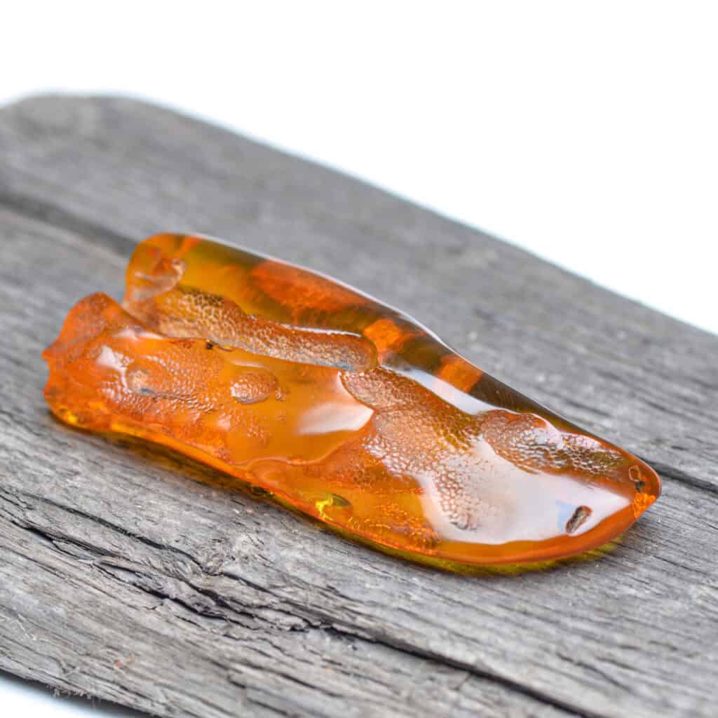 Polished Baltic amber piece with golden-orange hue resting on textured wood, showcasing natural beauty.