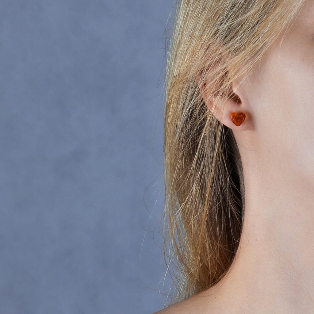 Close-up of a minimalist amber stud earring on a womans ear with blonde hair.