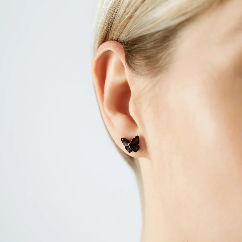 Black butterfly earring with intricate detail, elegant and reflective, highlighting delicate beauty on the ear.