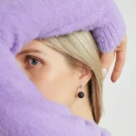 Close-up of a woman in a purple sweater with elegant black sphere earrings and captivating gaze.