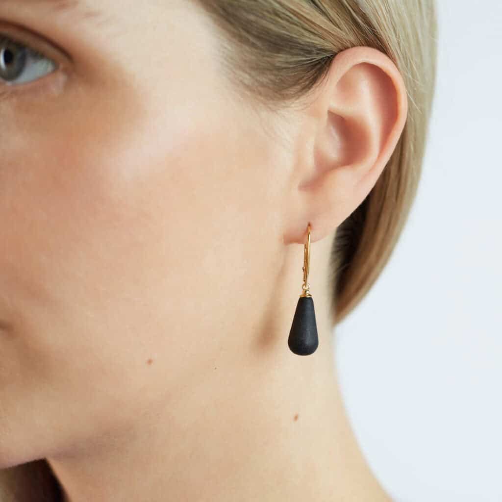 Elegant woman wearing black Baltic amber drop earring with gold chain detail.