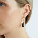 Elegant woman wearing black Baltic amber drop earring with gold chain detail.