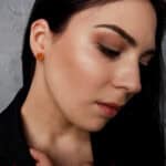 Elegant woman with neutral makeup, dark hair, and amber stud earrings in a serene profile view.