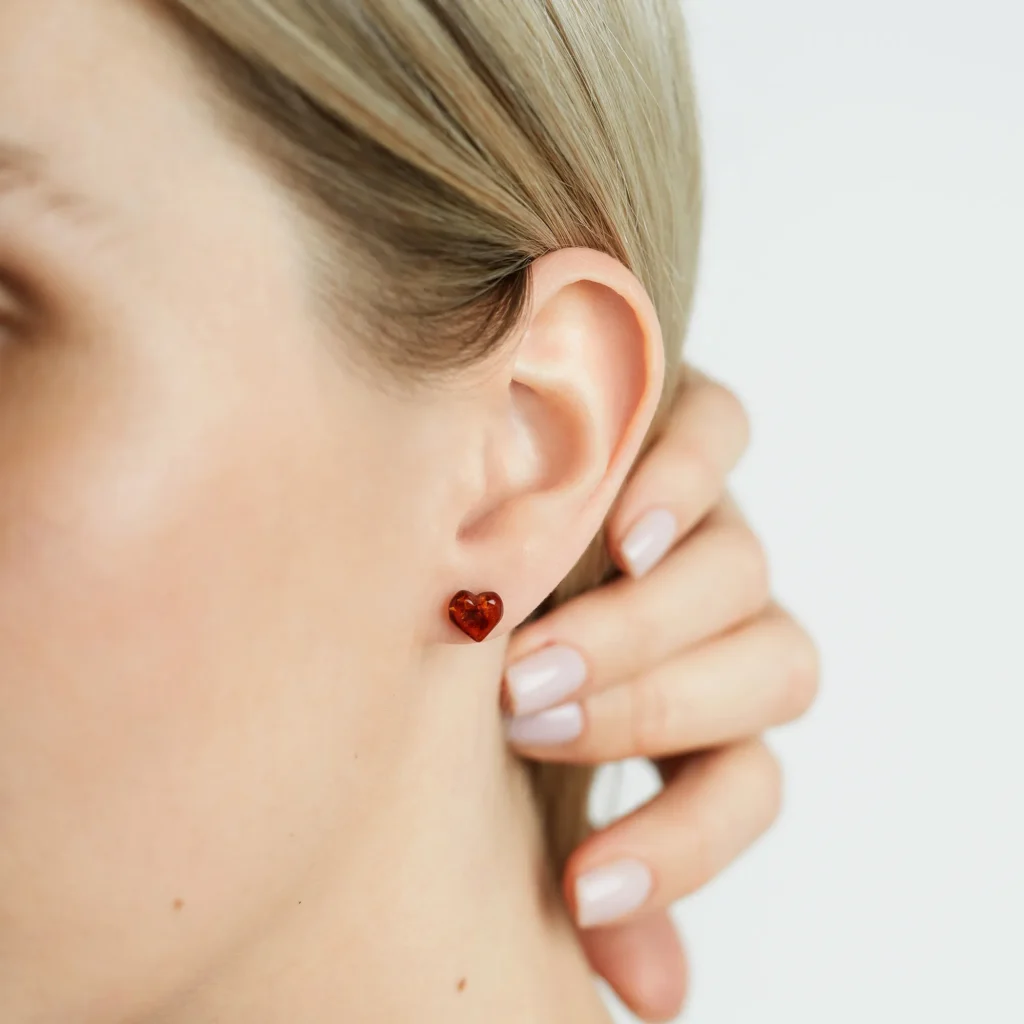 Close-up of a person wearing vibrant red heart-shaped amber earrings.