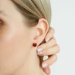 Close-up of a person wearing vibrant red heart-shaped amber earrings.