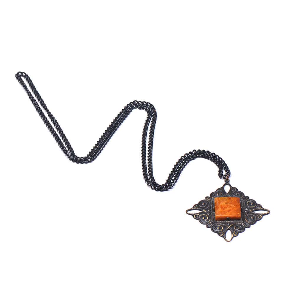 Vintage-style necklace with ornate pendant and vibrant orange center, dark metal chain, handcrafted elegance.