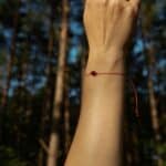 Natural amber cherry color bracelet with red string. On a woman's hand raised up in a nature scene