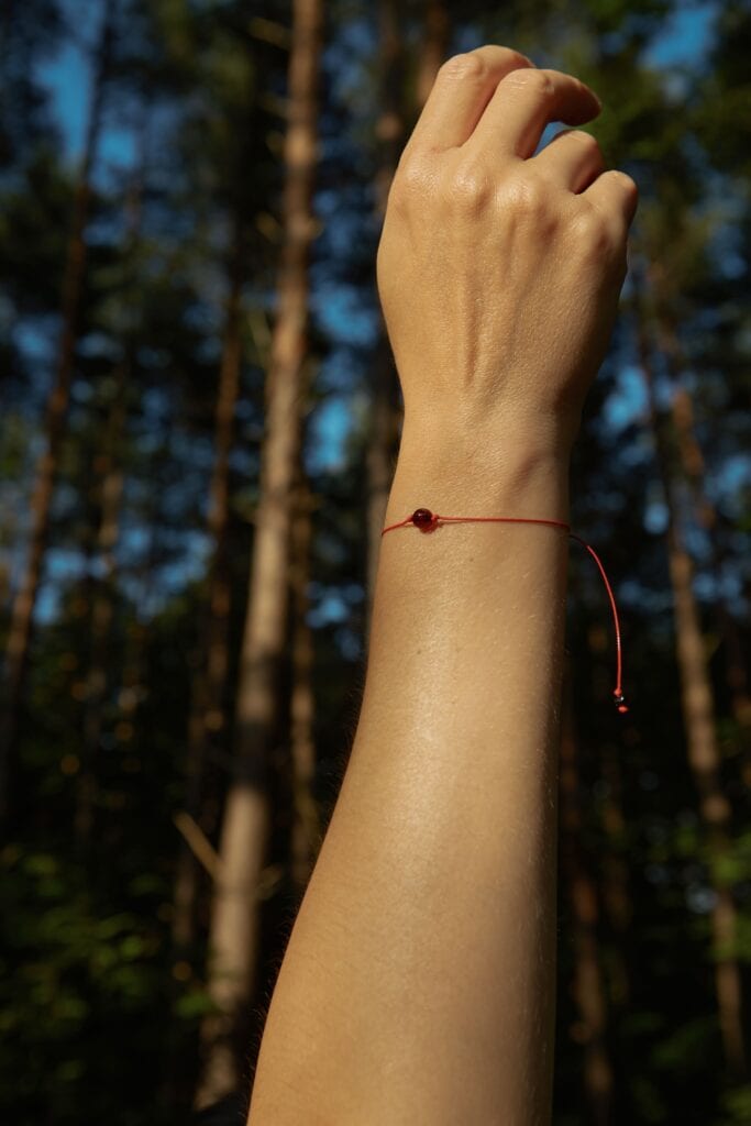 Natural amber cherry color bracelet with red string. On a woman's hand raised up in a nature scene