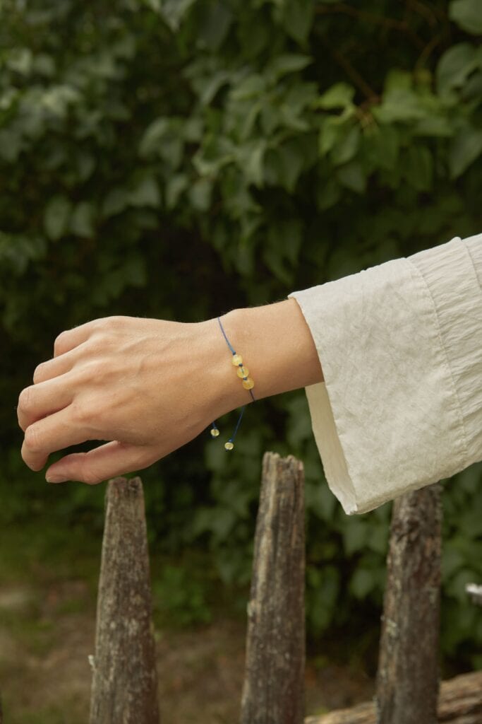 natural amber beads, three in the center with a blue string. On a woman's hand surrounded by nature
